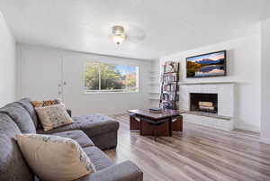 Living area featuring a ceiling fan, light wood-style floors, a textured ceiling, and a brick fireplace