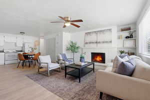 Living room with light wood-type flooring, a ceiling fan, and a brick fireplace