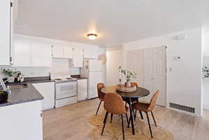 Kitchen with dark countertops, white appliances, white cabinetry, and light wood-style flooring