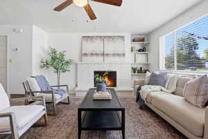 Living area featuring a ceiling fan, dark wood-style floors, and a brick fireplace