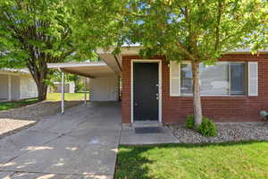 Entrance to property featuring a lawn, an attached carport, concrete driveway, and brick siding