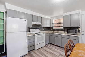 Kitchen with gray cabinets, white appliances, light countertops, light wood finished floors, and tasteful backsplash