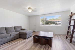 Living room featuring light wood-style flooring, ceiling fan, and a textured ceiling