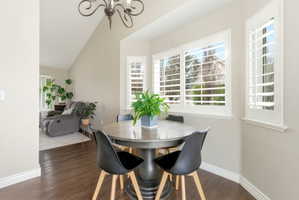 Dining space with dark wood finished floors, suspended lighting, and vaulted ceiling