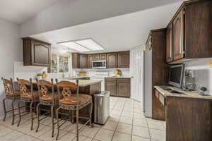 Kitchen featuring backsplash, a peninsula, dark wood finish cabinetry, a breakfast bar area, and light tile patterned flooring