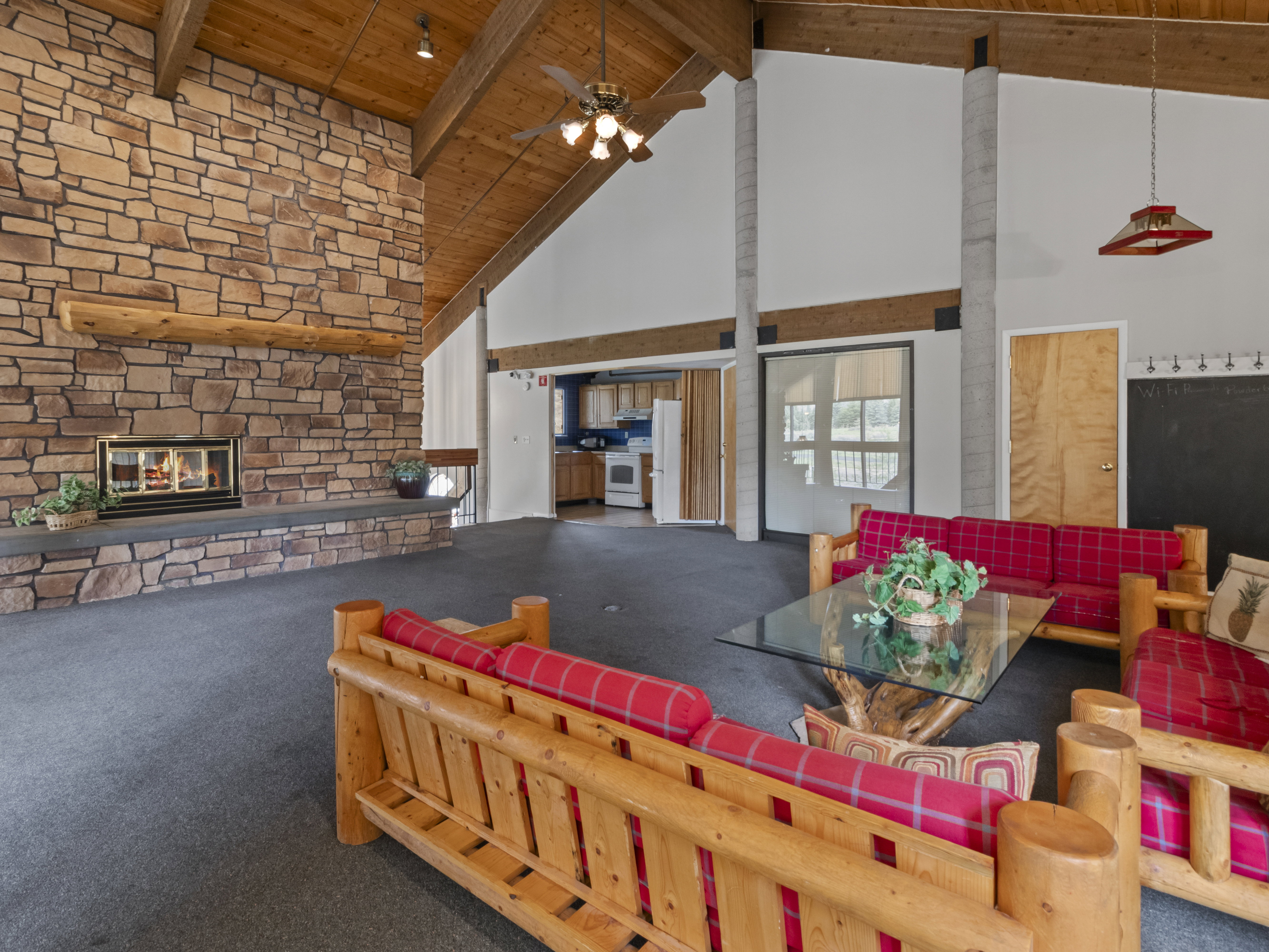 Living room with carpet, a stone fireplace, a high wooden beamed ceiling, and ceiling fan