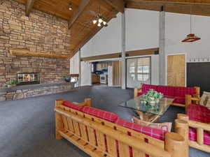 Living room with carpet, a stone fireplace, a high wooden beamed ceiling, and ceiling fan