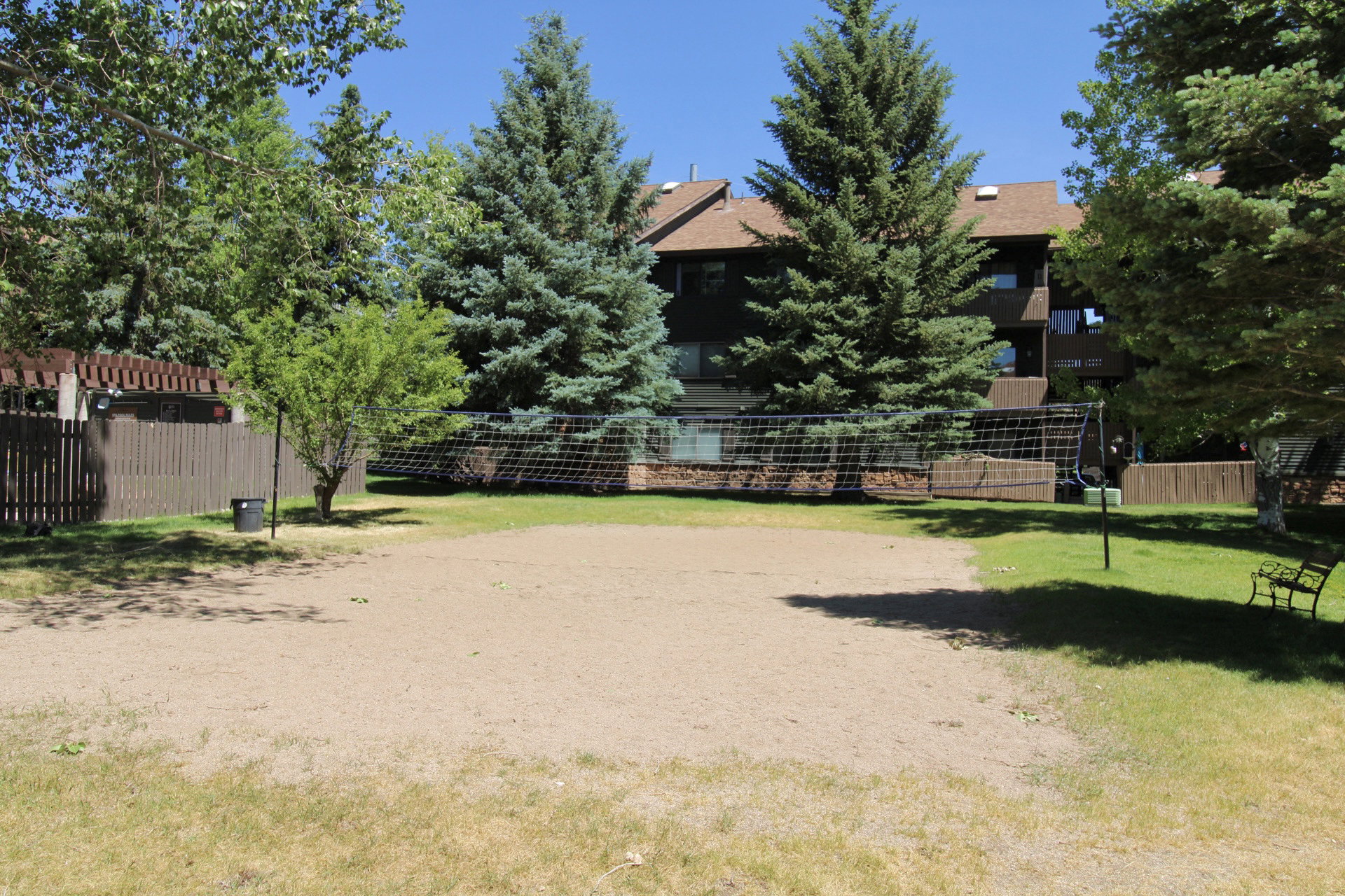 Sand court with a net, bordered by green lawn and mature trees
