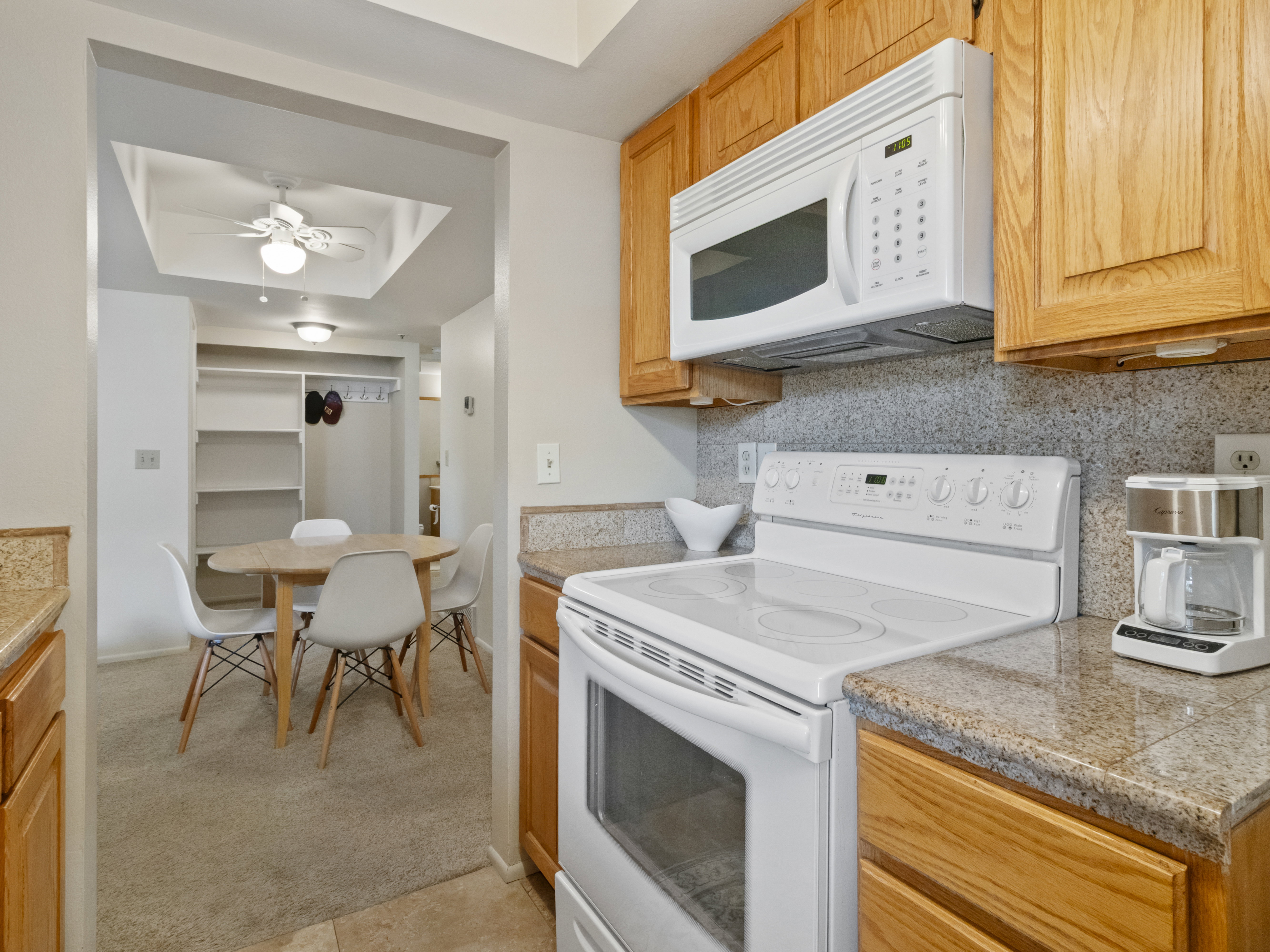 Kitchen featuring white appliances, a tray ceiling, tile counters, backsplash, and a ceiling fan