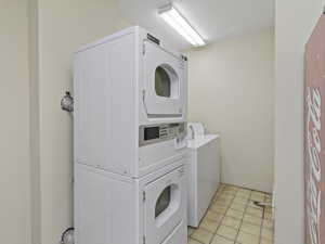 Laundry area with light tile patterned flooring and stacked washer / dryer