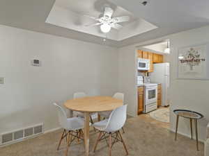 Dining area featuring a ceiling fan, a raised ceiling, and light colored carpet