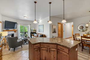 Kitchen featuring decorative light fixtures, open floor plan, wood finish cabinetry, a kitchen island, and a fireplace