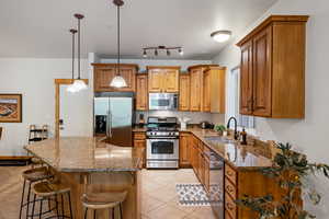 Kitchen featuring dark stone counters, stainless steel appliances, wood finish cabinetry, a kitchen island, and a kitchen bar
