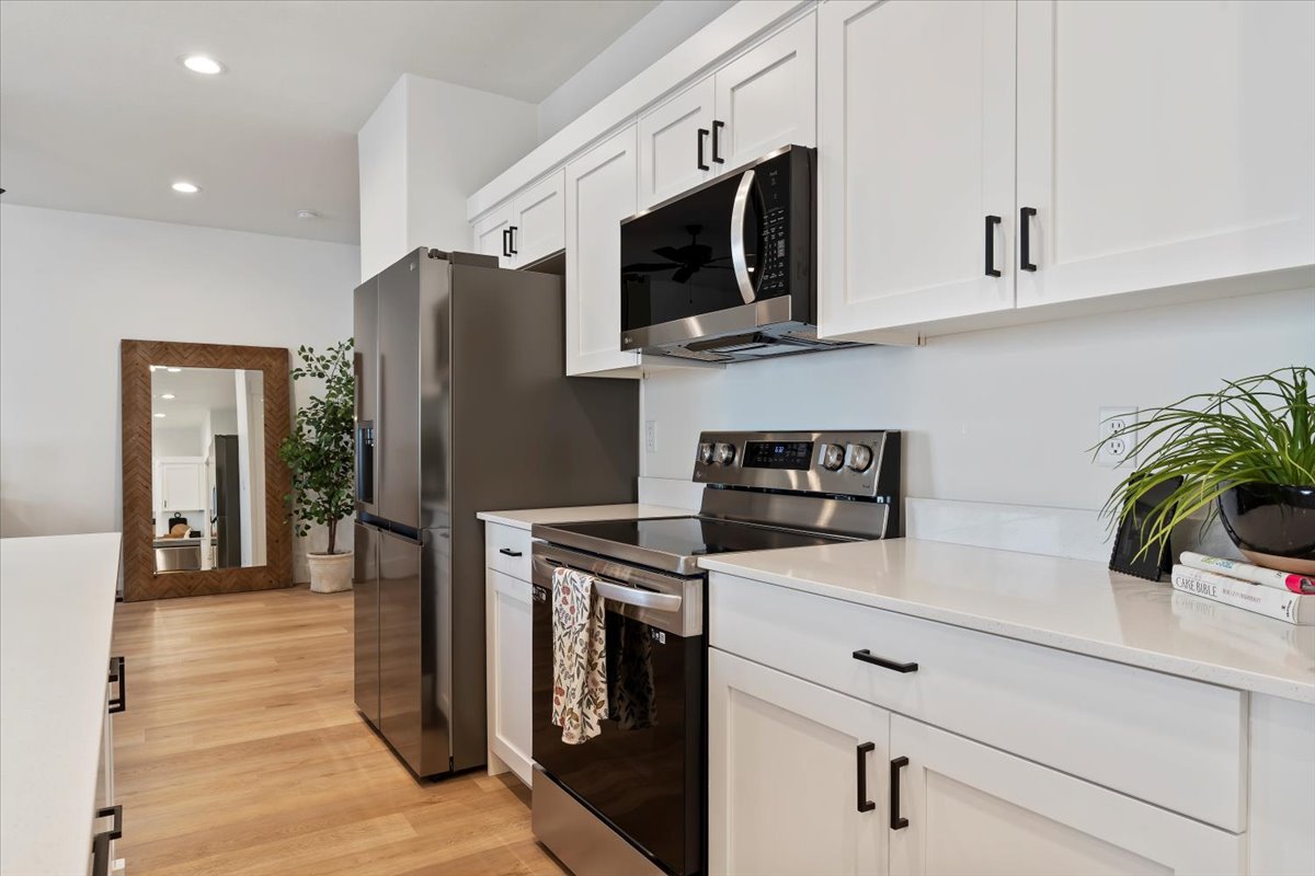 Kitchen with stainless steel appliances, recessed lighting, white cabinets, light wood-type flooring, and light stone counters
