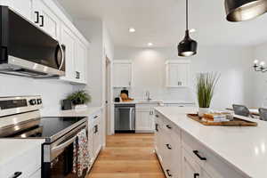Kitchen featuring stainless steel appliances, hanging light fixtures, light wood finished floors, white cabinets, and light stone counters