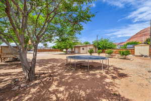 Fenced backyard featuring a trampoline and a storage unit