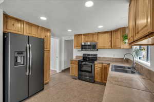 Kitchen featuring stainless steel appliances, recessed lighting, light tile patterned floors, tile counters, and wood finish cabinetry