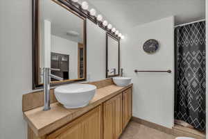 Bathroom with curtained shower, double vanity, light tile patterned floors, and a textured ceiling