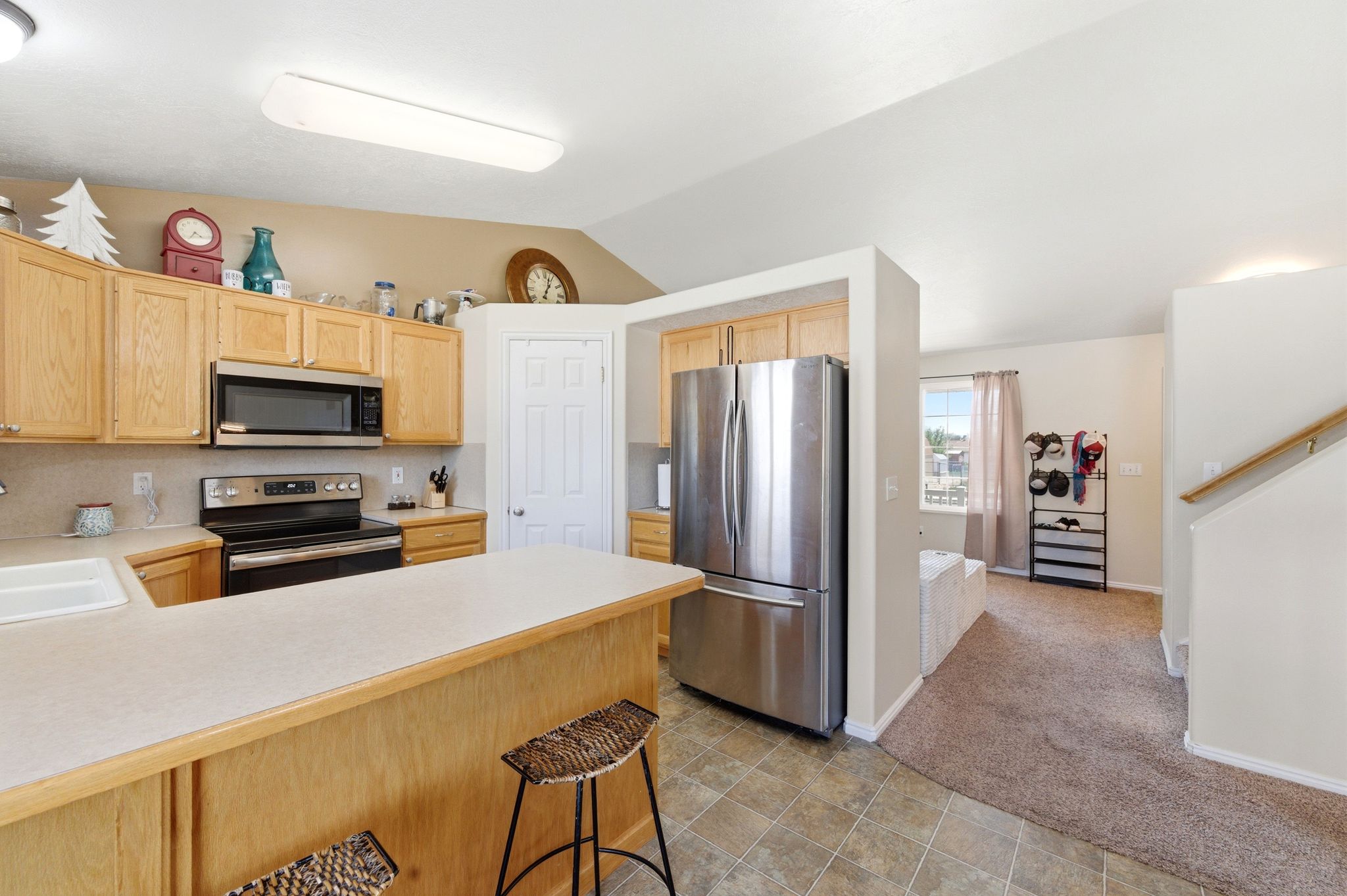 Kitchen featuring light countertops, stainless steel appliances, light colored carpet, light wood finish cabinets, and vaulted ceiling