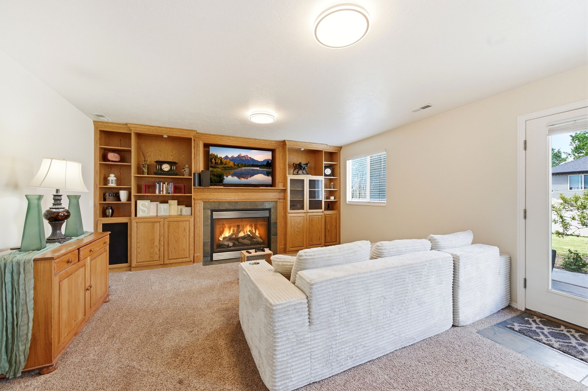 Living area with light colored carpet, a tiled fireplace, and built in shelves