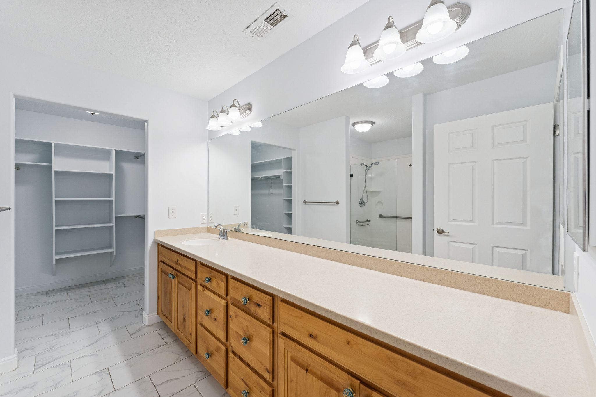 Bathroom featuring a stall shower, a walk in closet, vanity, and light marble finish flooring
