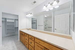 Bathroom featuring a stall shower, a walk in closet, vanity, and light marble finish flooring
