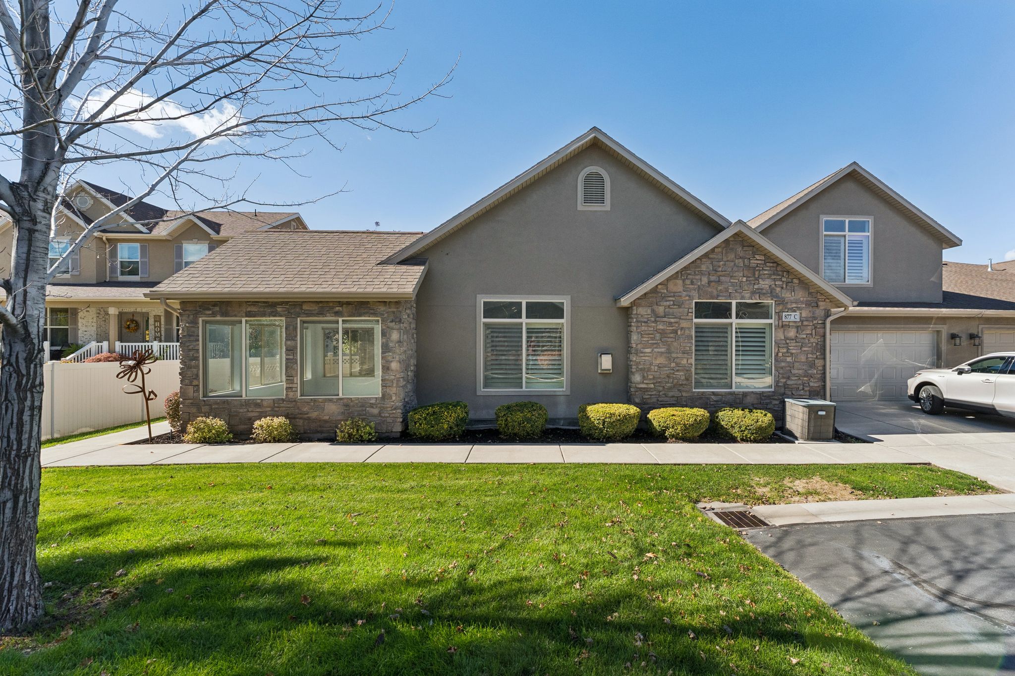 Craftsman-style home featuring stucco siding, stone siding, a garage, and driveway