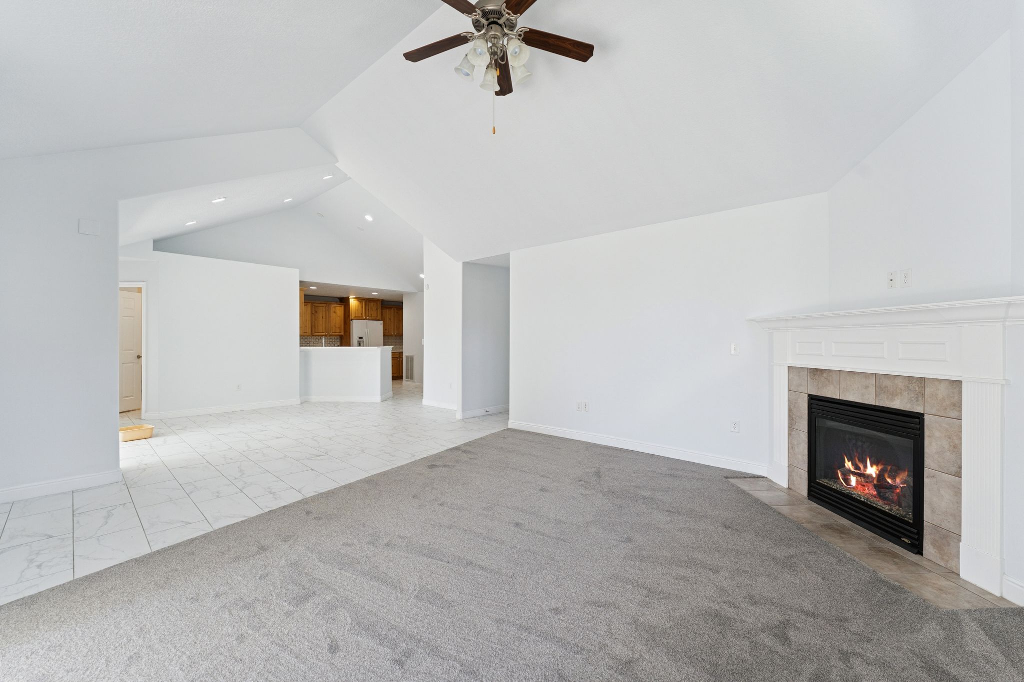 Unfurnished living room featuring ceiling fan, a fireplace, a high ceiling, and light marble finish flooring