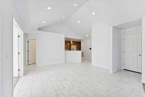 Unfurnished living room featuring light marble finish flooring, vaulted ceiling, and recessed lighting