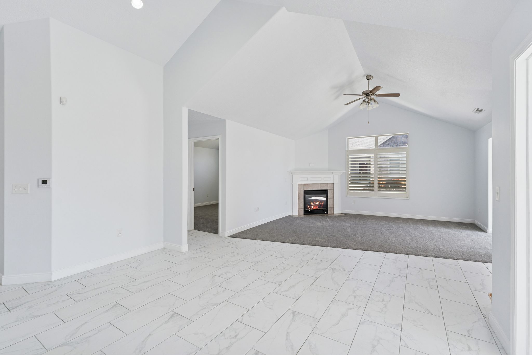 Unfurnished living room featuring a fireplace, light marble finish floors, and ceiling fan