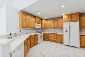 Kitchen with white appliances, light marble finish flooring, light stone countertops, and a peninsula
