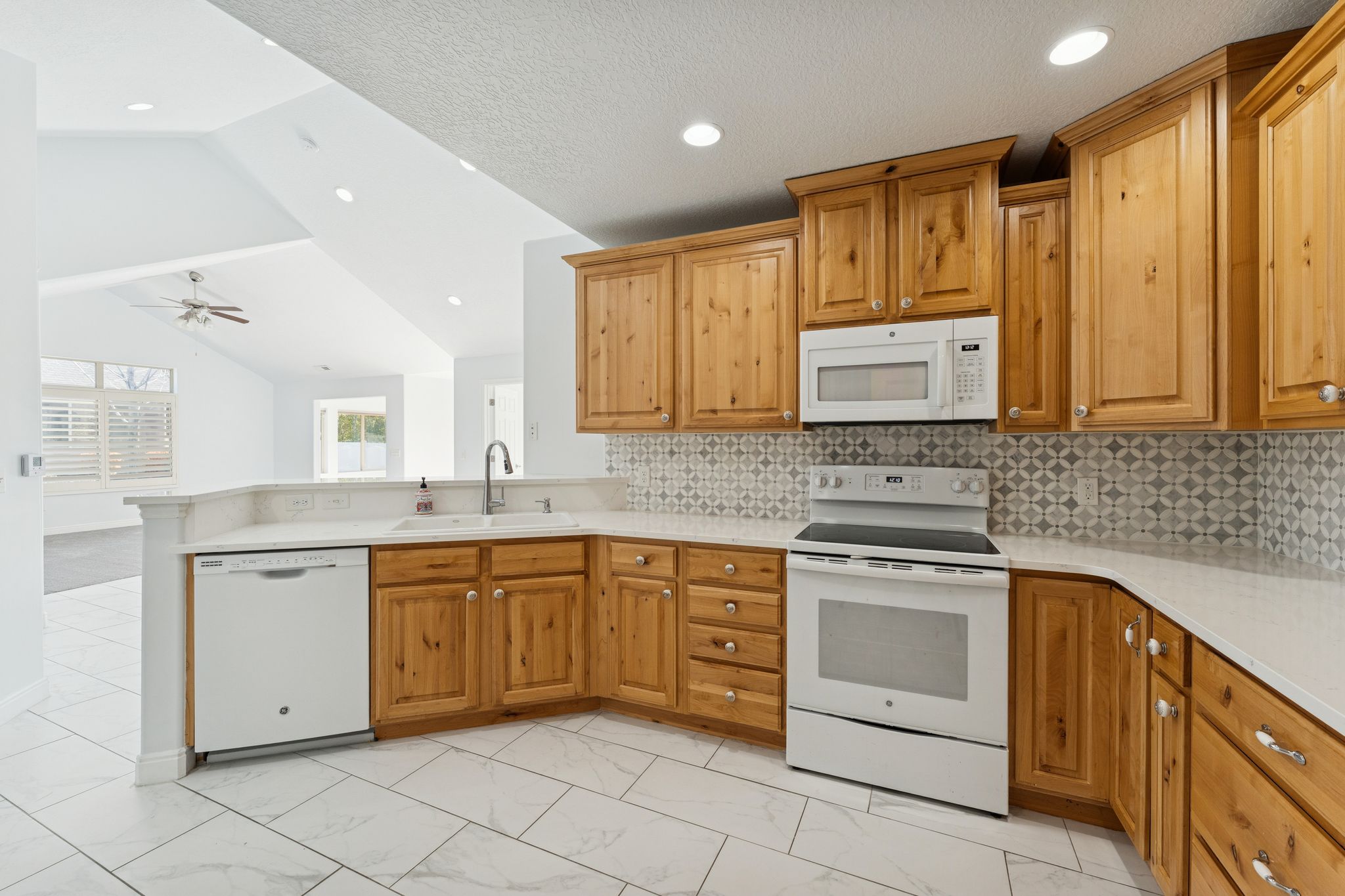 Kitchen featuring white appliances, wood finish cabinets, a peninsula, light stone counters, and recessed lighting