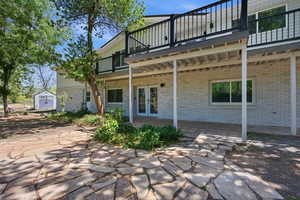 Rear view of house with a balcony, a storage unit, a patio, brick siding, and french doors