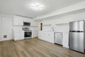 Kitchen featuring stainless steel appliances, white cabinetry, light countertops, light wood-style floors, and open shelves