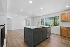 Kitchen featuring light wood-type flooring, a kitchen island with sink, dual tone cabinetry, recessed lighting, and arched walkways
