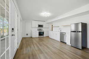 Kitchen with stainless steel appliances, light countertops, white cabinets, and light wood-style flooring