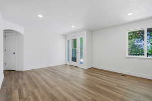 Empty room with light wood-style floors, arched walkways, and recessed lighting