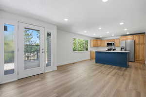 Dual tone kitchen featuring light countertops, stainless steel appliances, a kitchen island with sink, light wood-style flooring, and recessed lighting