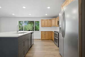 Two tone kitchen with stainless steel appliances, two tone color scheme, light wood-style floors, recessed lighting, and an island with sink