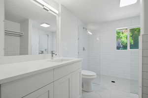 Full bath featuring vanity, a tile shower, and tile walls