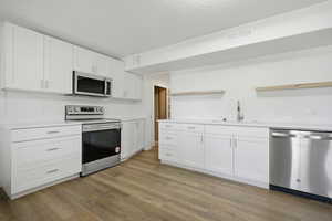 Kitchen featuring stainless steel appliances, white cabinetry, light wood-type flooring, and open shelves