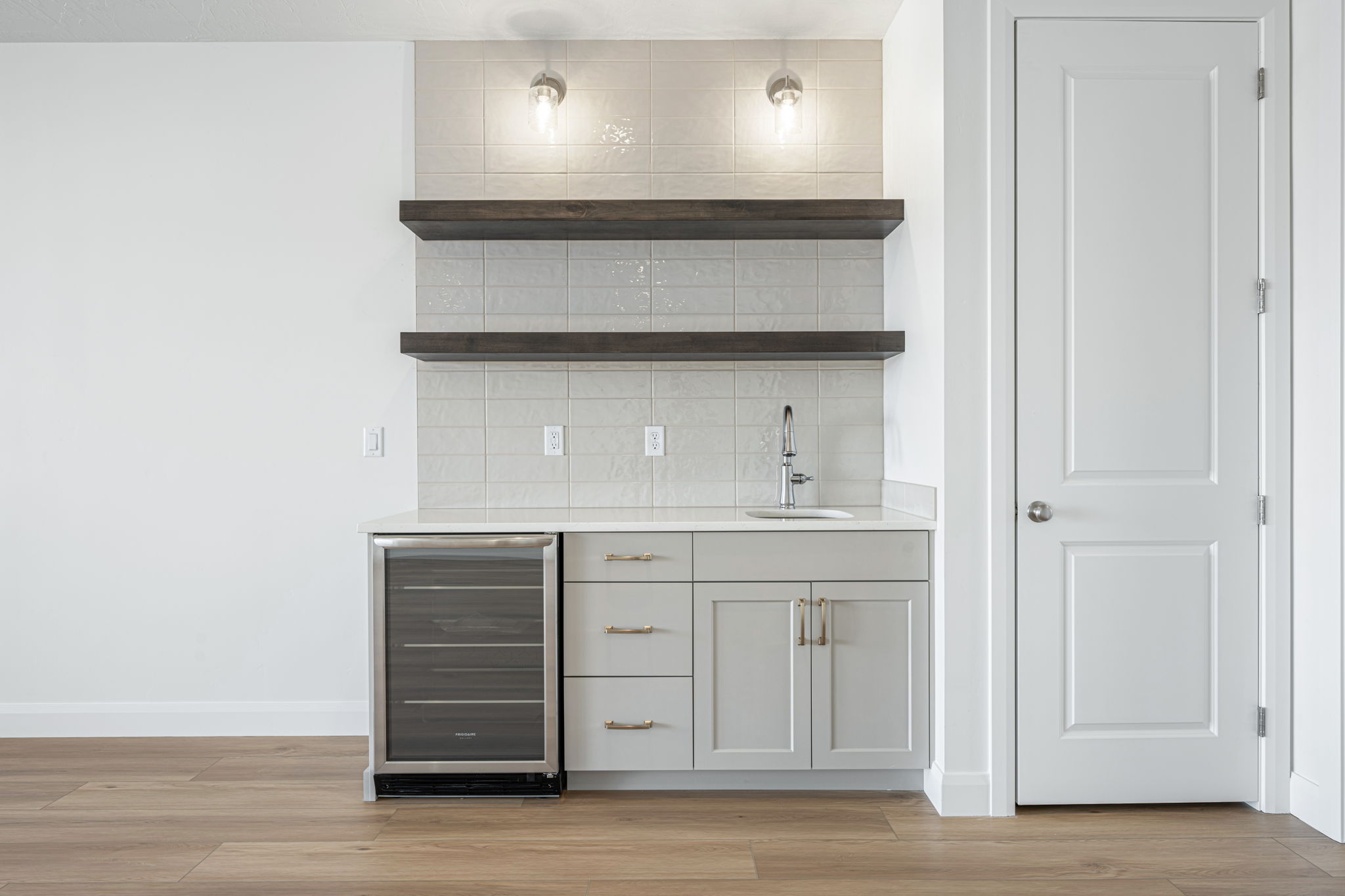 Built-in wet bar featuring light grey cabinetry, a stainless steel sink with a chrome faucet, a beverage refrigerator, and open wood shelving