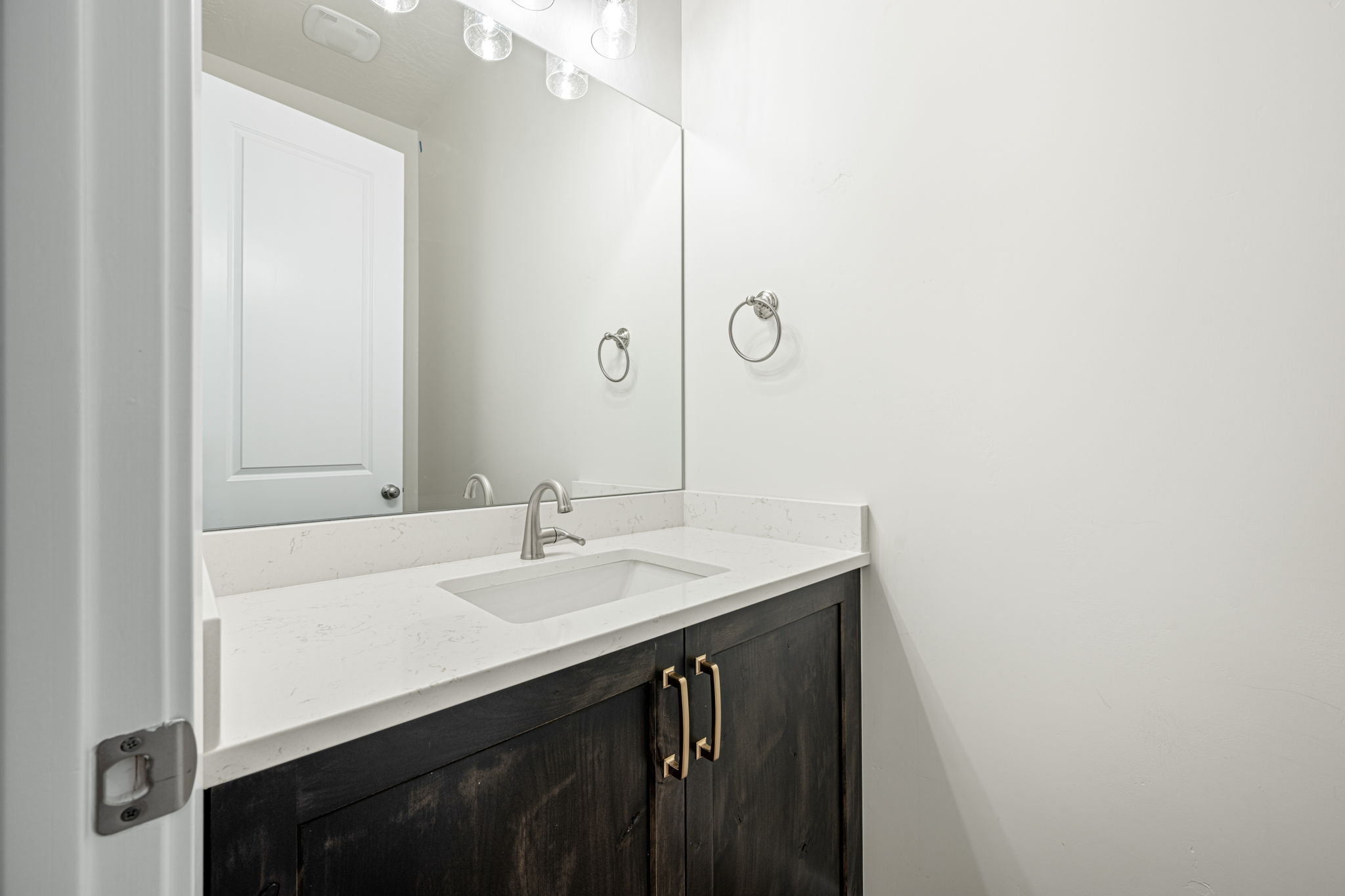 Vanity with dark wood-finish cabinetry, brushed nickel hardware, and a white countertop featuring an integrated rectangular sink