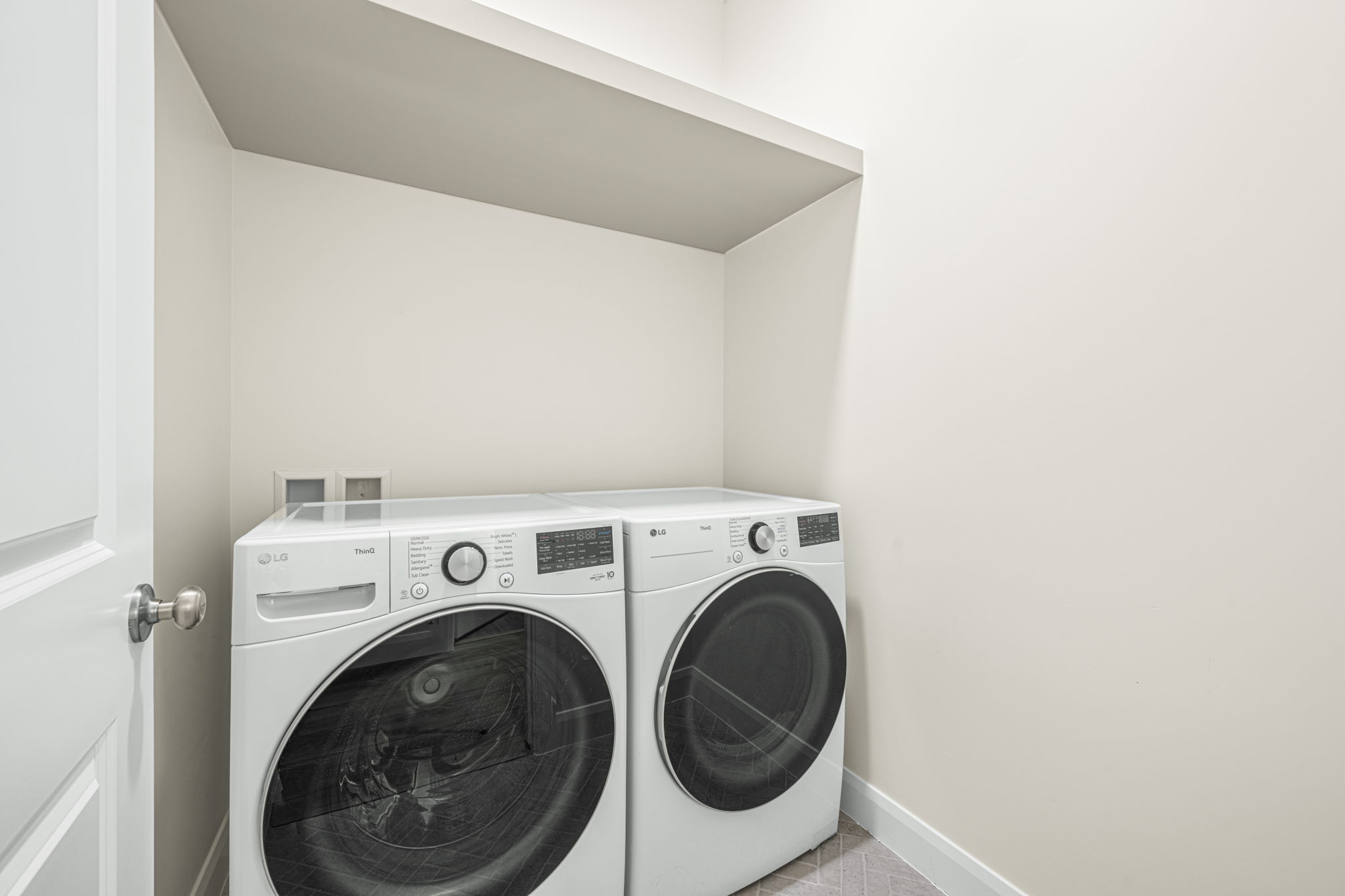 Dedicated laundry space featuring a white paneled door with brushed nickel hardware, light neutral walls, and a built-in overhead shelf