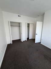 Unfurnished bedroom featuring two closets and dark colored carpet