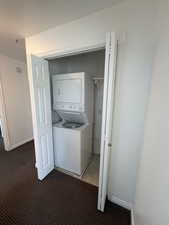 Laundry area featuring stacked washer and dryer and light colored carpet