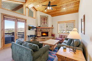 Living room with a stone fireplace, a ceiling fan, a vaulted wood ceiling, and carpet
