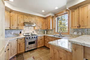 Kitchen featuring designer stove, light stone counters, light wood finish cabinets, decorative backsplash, and recessed lighting
