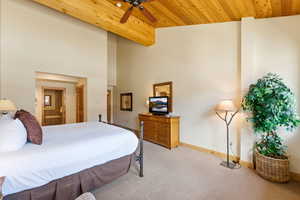 Bedroom featuring light carpet, connected bathroom, a ceiling fan, and a high wooden ceiling