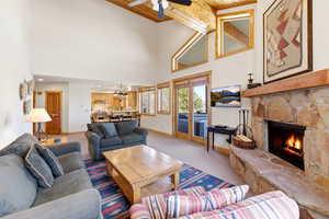 Carpeted living room featuring a fireplace, ceiling fan, hanging lights, and a vaulted wood ceiling
